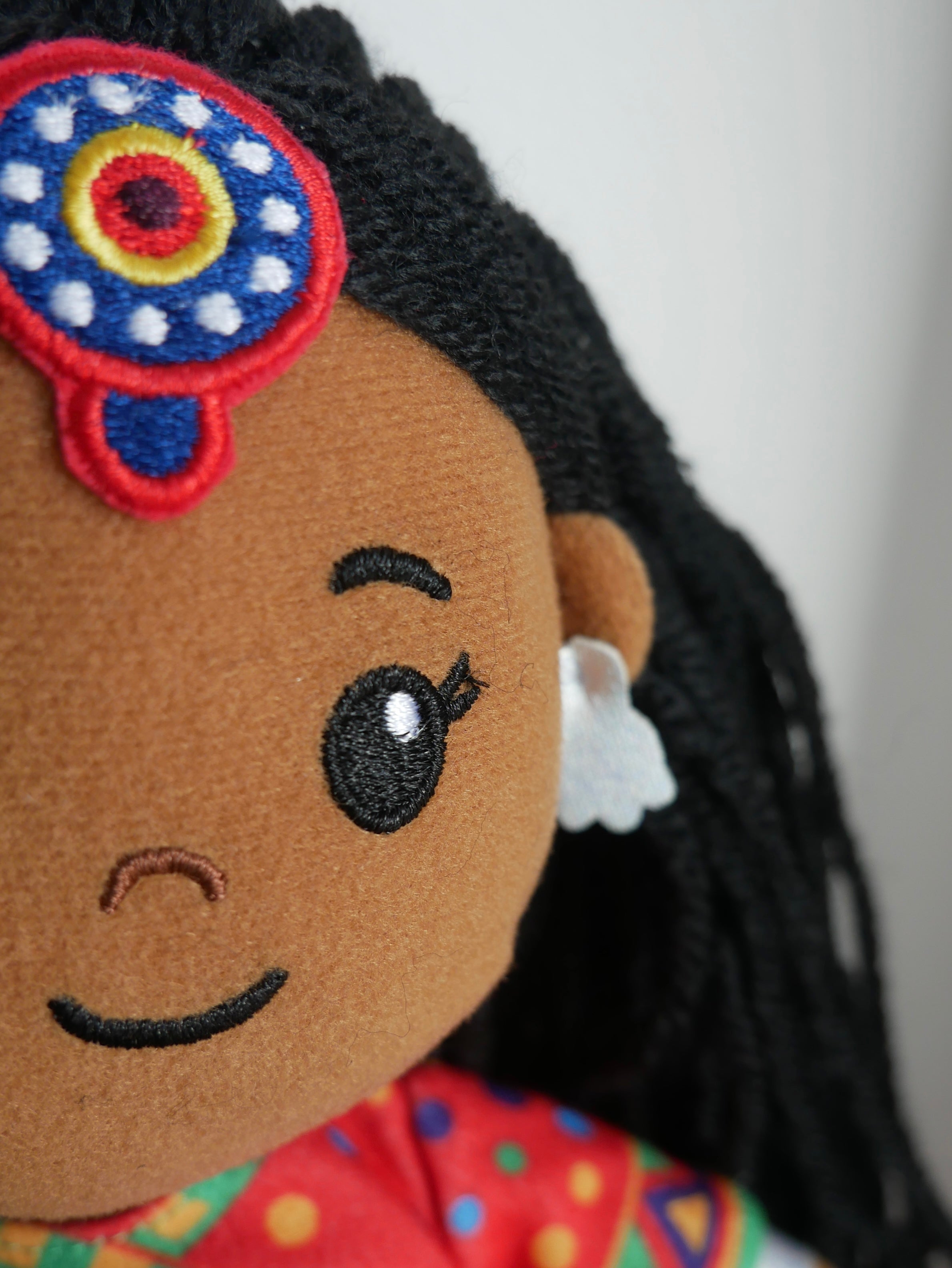Close-up of a doll with embroidered face and colorful hair accessory.